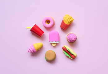 A variety of toy fast food and different sweets in miniature with shadows on a soft pink background.