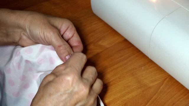 an adult woman seamstress sews impales the fabric with a needle. Hands close up. grandma makes a smooth hand stitch. Making clothes and sewing colored bed linen at home or in a garment factory