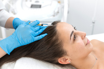 Close-up, the beautician makes injections of vitamins into the scalp for strengthening the hair.