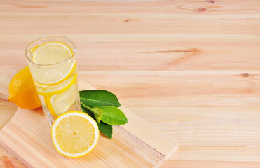 Glasses of lemonade with lemons and green leaves on wooden background.