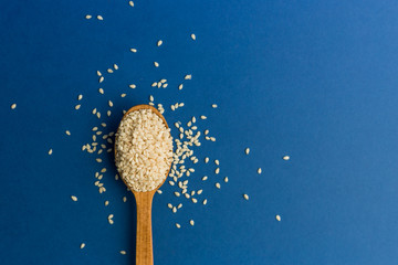 White sesame seeds in spoon on blue background. Color of the year 2020. Healthy food and drink...
