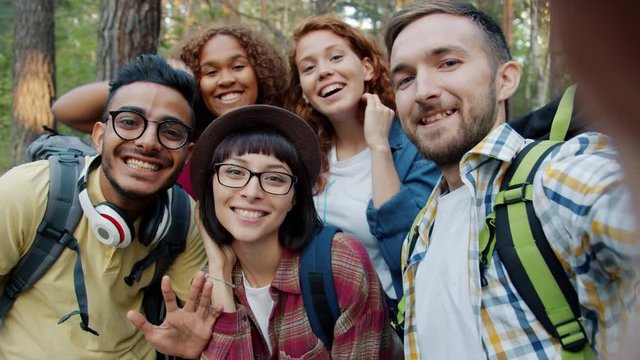 POV of cheerful girls and guys taking selfie in woods holding camera having fun together, beautiful young people are posing for self-portrait. Nature and devices concept.
