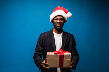 Young african american man holding gift boxes in hands on isolated blue background