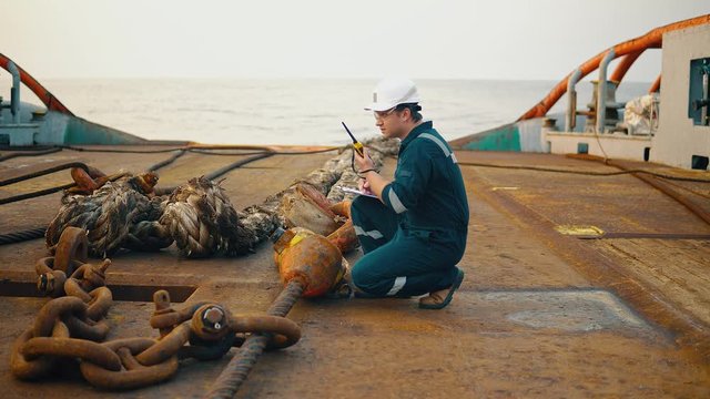 Marine chief officer or chief mate on deck of ship or vessel. He fills up ahts vessel checklist. Ship routine paperwork. He holds VHF walkie-talkie radio in hands.