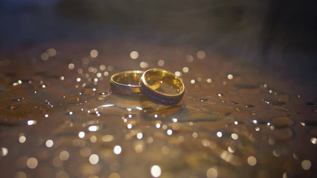 Wedding rings lying on dark surface with reflection and water. Shining with light close up macro.