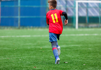 Boys in red and blue sportswear plays football on field, dribbles ball. Young soccer players with ball on green grass. Training, football, active lifestyle for kids concept
