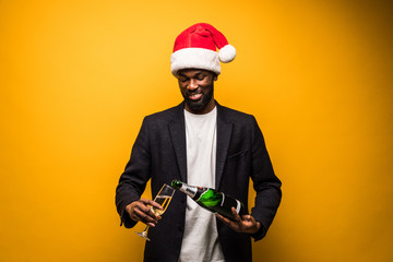 Young african man in santa hat holding champange and drink isolated on yellow background
