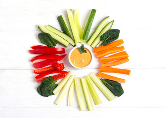 Diet raw sticks of celery,carrots,cucumber and red bell paper with sauce on the white wooden...