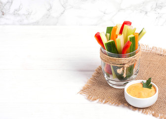 Diet raw sticks of celery,carrots,cucumber and red bell paper in glass whith sauce on thr white...