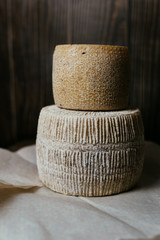 Different homemade cheeses on a dark wooden background. Pieces and cheese heads of kravot, manchego, Paramezan. Goat and cow cheese on baking paper. Handwork. Close up