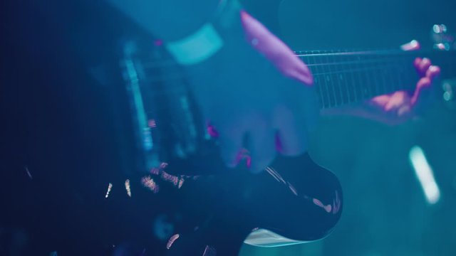 Close up shot of rock musician with guitar in stage lights and smoke. Slow motion playing