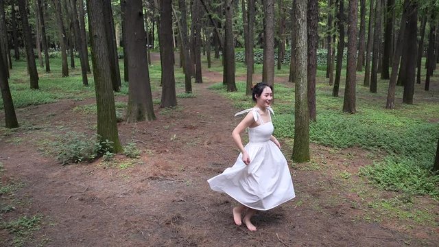 High angle view of beautiful Chinese young woman in white dress dancing in forest park, carefree girl rotating joyfully, enjoy her self in nature, super slow motion, summer concept.