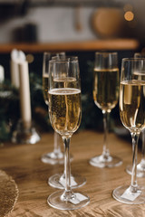 Group of glasses of luxury champagne on a wooden table. White wine in glasses of champagne against the background of a Christmas tree and garland lights