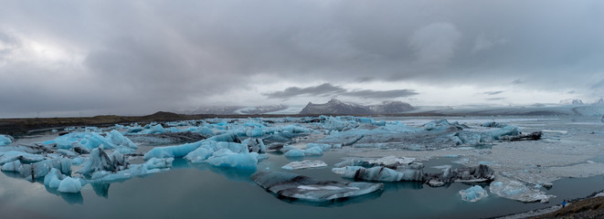 Panoramic view of glacier lagoon with glacial and mountains in the background, black and blue ice form icebergs