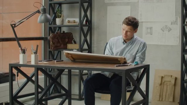 Architect man sits at drafting table in modern industrial office during the day
