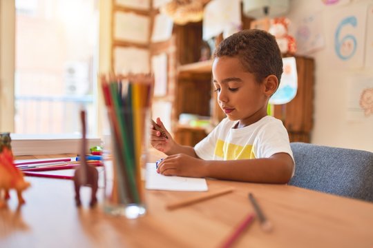 Beautiful african american toddler sitting painting car toy using marker pen on desk at kindergarten