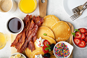 Big pancake breakfast table with berries, bacon and maple syrup