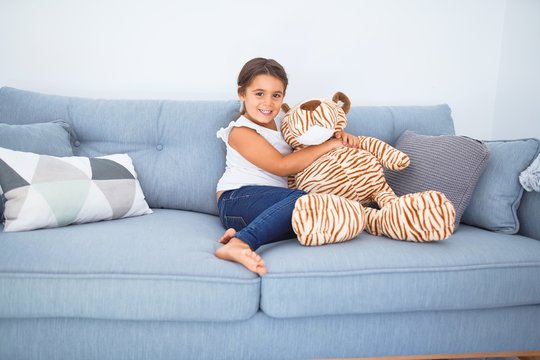 Adorable toddler smiling happy. Sitting on the sofa hugging doll at home