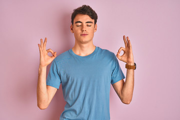 Teenager boy wearing casual t-shirt standing over blue isolated background relax and smiling with eyes closed doing meditation gesture with fingers. Yoga concept.