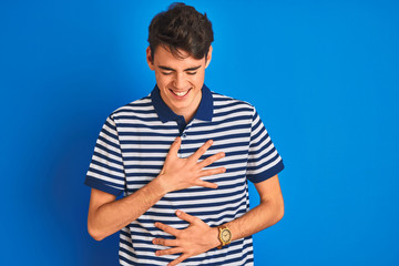 Teenager boy wearing casual t-shirt standing over blue isolated background smiling and laughing hard out loud because funny crazy joke with hands on body.