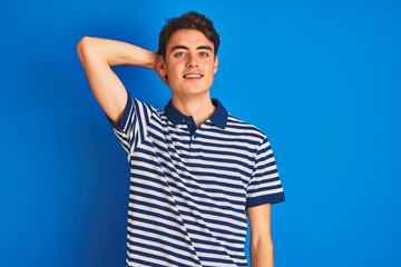 Teenager boy wearing casual t-shirt standing over blue isolated background smiling confident touching hair with hand up gesture, posing attractive and fashionable