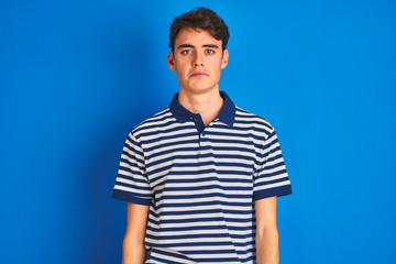 Teenager boy wearing casual t-shirt standing over blue isolated background depressed and worry for distress, crying angry and afraid. Sad expression.