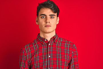 Teenager boy wearing red shirt standing over isolated background with serious expression on face....