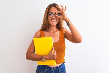Young beautiful redhead woman wearing glasses reading a book over isolated background with happy face smiling doing ok sign with hand on eye looking through fingers