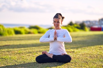 Fototapeta premium Young beautiful sportwoman smiling happy practicing yoga. Coach sitting with smile on faceteaching prayer pose at park