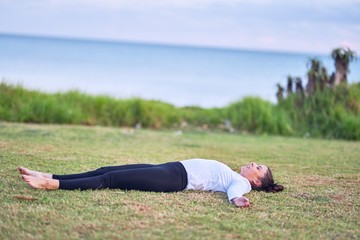 Fototapeta na wymiar Young beautiful sportwoman practicing yoga. Coach lying down teaching corpose pose at park