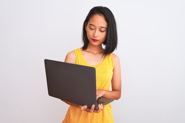 Young beautiful chinese woman using laptop standing over isolated white background with a confident expression on smart face thinking serious