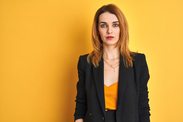 Redhead caucasian business woman over yellow isolated background with serious expression on face. Simple and natural looking at the camera.