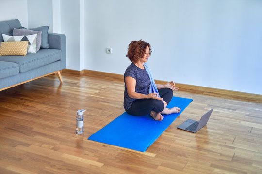 Middle age beautiful sportswoman smilig happy. Sitting on mat with smile on face using laptop at home
