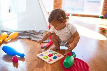 Adorable toddler learning numbers using maths puzzle around lots of toys at kindergarten