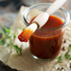 Homemade sweet and spicy barbeque sauce with a basting brush in a jar
