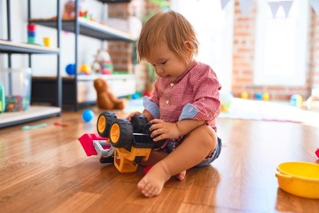 Adorable toddler playing with tractor around lots of toys at kindergarten