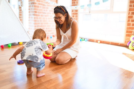 Beautiful teacher and toddler building pyramid using hoops around lots of toys at kindergarten