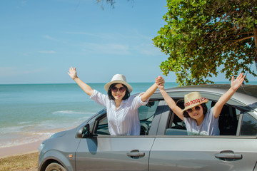 Summer Vacation and Car Trip Concept : Family car trip at the sea, Woman and child cheerful raising their hands up and feeling happiness in silver car with seascape in the background.