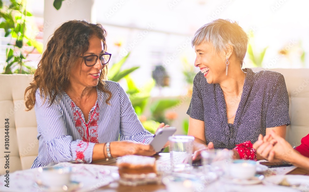 Wall mural meeting of middle age women having lunch and drinking coffee. mature friends smiling happy using sma