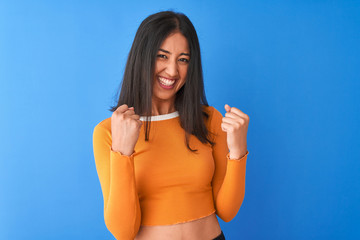 Young beautiful chinese woman wearing orange t-shirt standing over isolated blue background very...