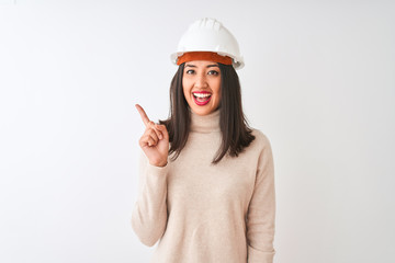 Young chinese architect woman wearing security helmet over isolated white background with a big smile on face, pointing with hand and finger to the side looking at the camera.