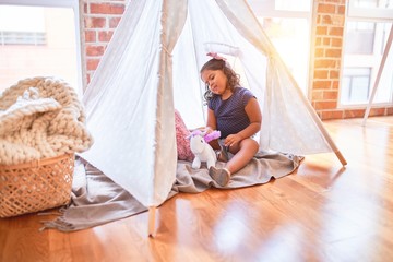 Beautiful toddler girl sitting on the floor playing with unicorn inside tipi at kindergarten © Krakenimages.com