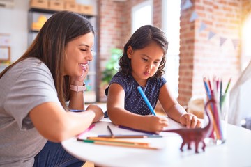 Beautiful teacher and toddler girl drawing draw using colored pencils at kindergarten