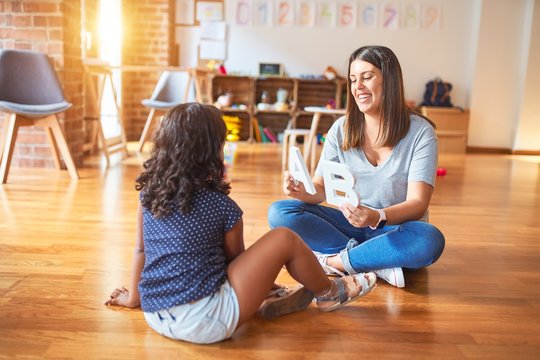 Beautiful teacher teaching alphabet to student toddler girl at kindergarten