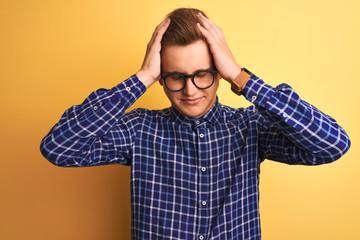 Young handsome man wearing casual shirt and glasses over isolated yellow background suffering from headache desperate and stressed because pain and migraine. Hands on head.