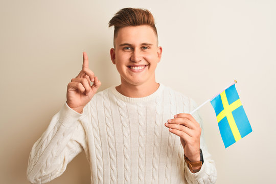 Young handsome man holding Sweadish Sweden flag over isolated white background surprised with an idea or question pointing finger with happy face, number one