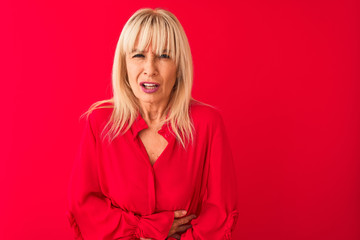 Fototapeta premium Middle age woman wearing elegant shirt standing over isolated red background with hand on stomach because nausea, painful disease feeling unwell. Ache concept.