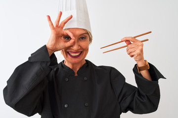 Middle age chef woman wearing cap holding chopsticks over isolated white background with happy face smiling doing ok sign with hand on eye looking through fingers