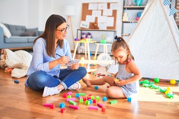 Fototapeta premium Młoda terapeuta mówi i leczy dziecko, doradca i korekta zachowania w kasie pedagoga, robi notatki na schowku