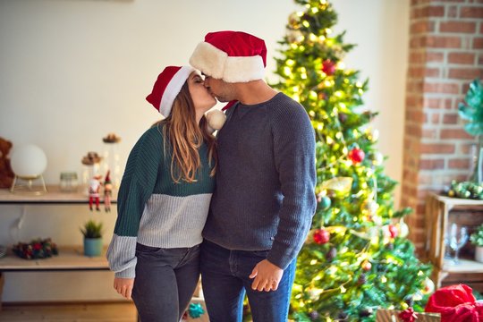 Young beautiful couple smiling happy and confident. Wearing santa claus hat standing around christmas tree at home